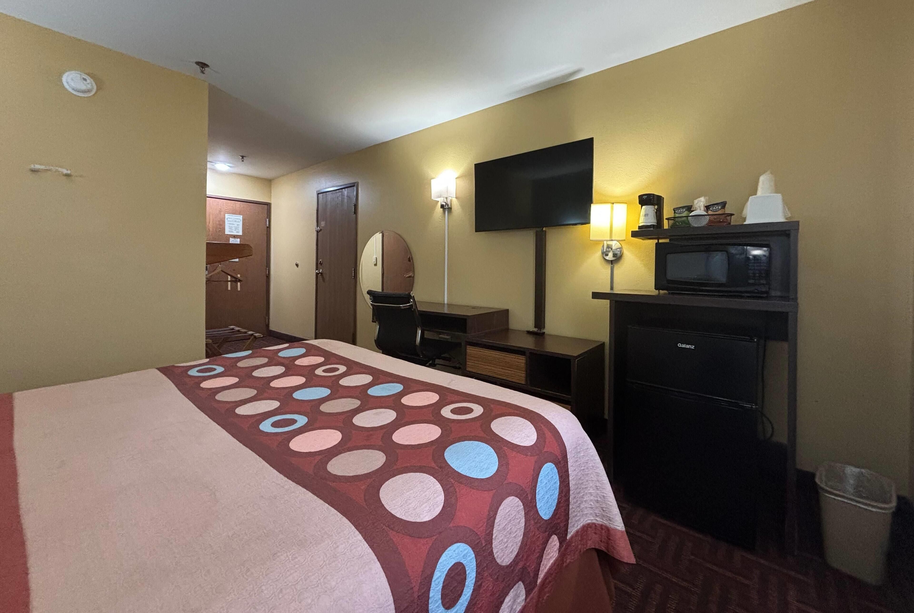 A hotel room with a bed, a desk, a television, a microwave, and a trash can.