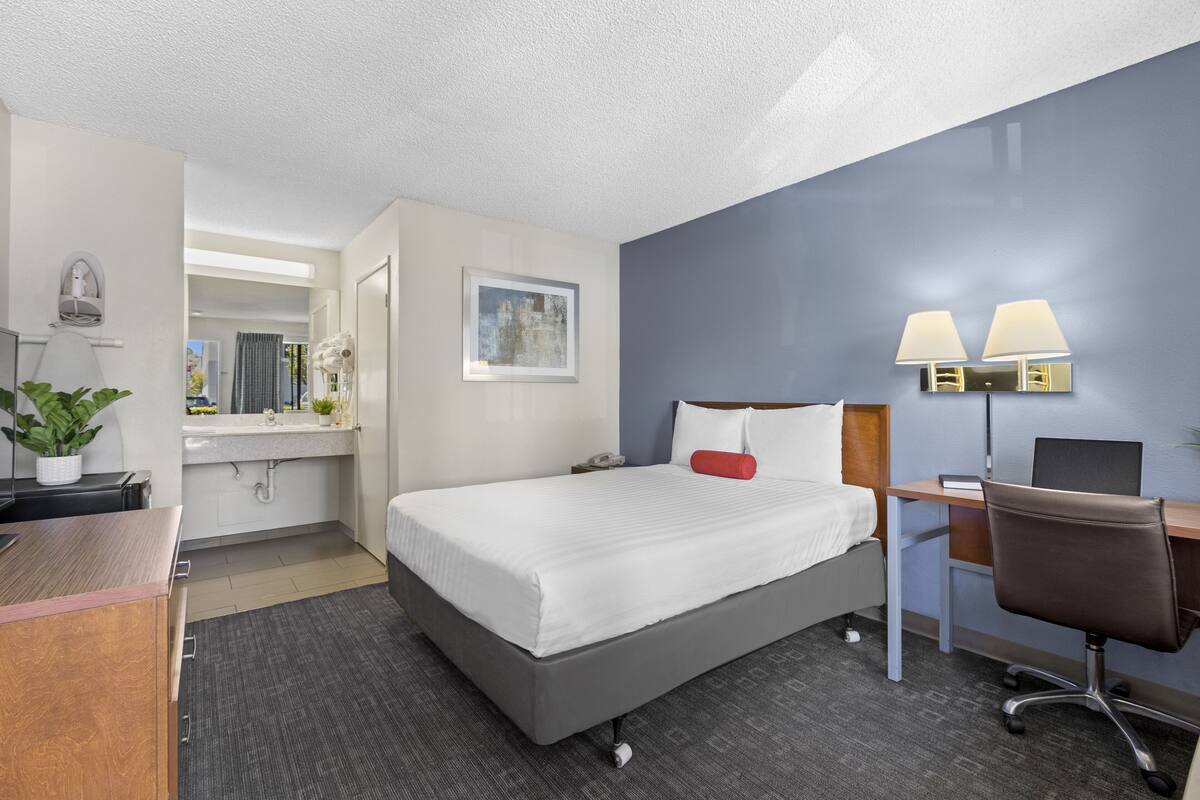 A hotel room with a bed, desk, chair, and a bathroom visible through an open door.