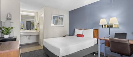 A hotel room with a bed, desk, chair, and a bathroom visible through an open door.