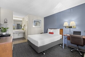Habitación de hotel con cama, escritorio, silla y baño visible a través de una puerta abierta.