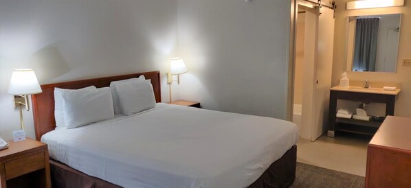A hotel room with a bed, bedside lamps, a nightstand, a bathroom with a sink and mirror, and a small wooden dresser. - Good Nite Inn - Calabasas (Agoura Hills)