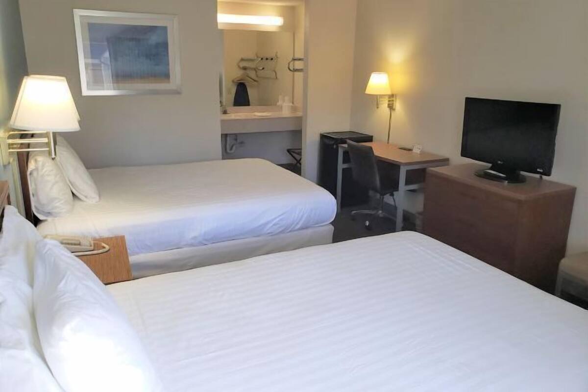 Quarto de hotel com duas camas, uma escrivaninha com computador, televisão e espelho.