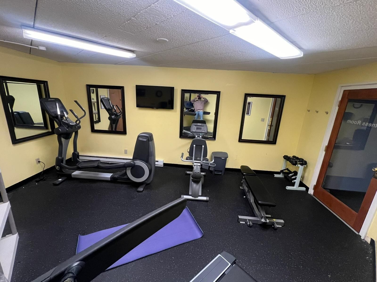 Un gimnasio con equipo de ejercicio, espejos y una puerta que indica "ROOM 222".