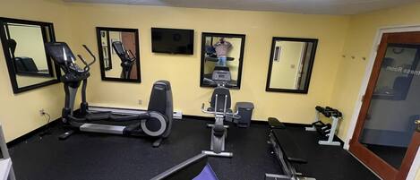 Un gimnasio con equipo de ejercicio, espejos y una puerta que indica "ROOM 222".
