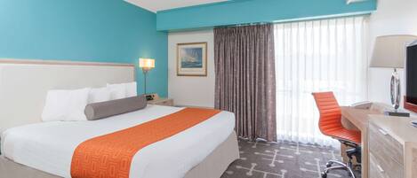 A hotel room with a large bed, a desk, a chair, a television, and a window with curtains.