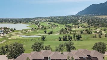 A golf course with a lake, mountains, and a building with multiple floors and balconies.
