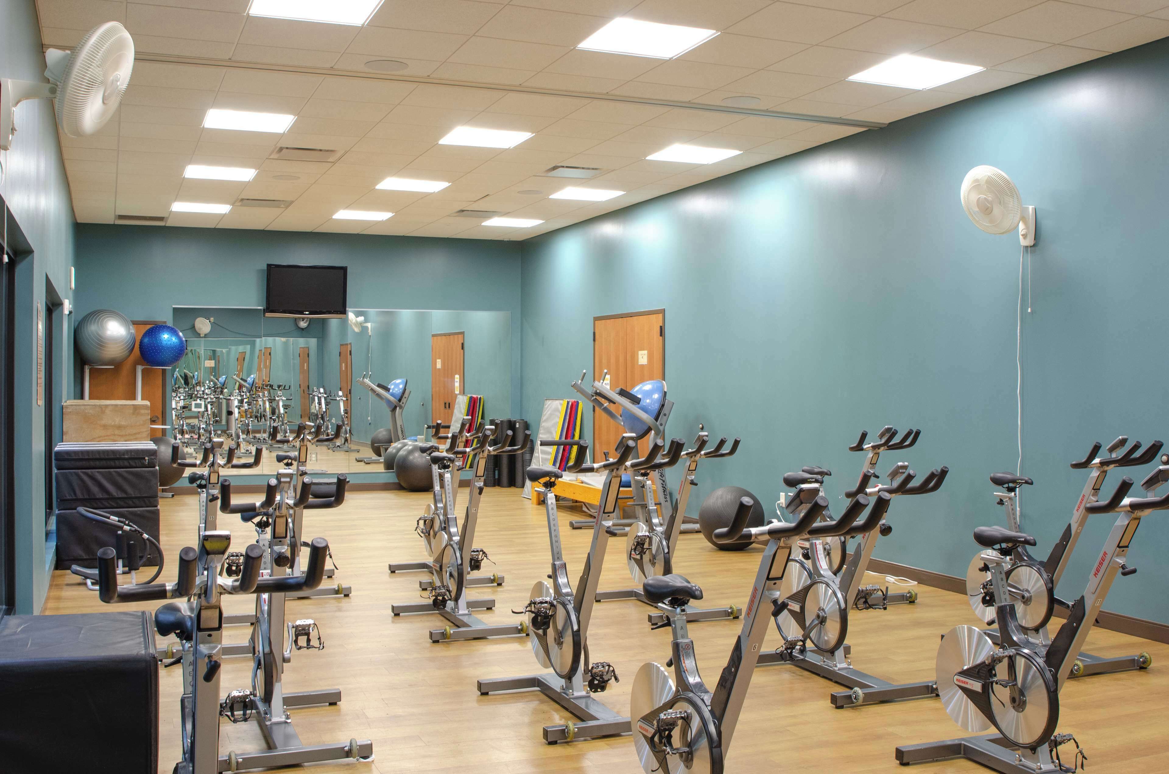 Een sportschool met meerdere hometrainers, een spiegel en diverse fitnessapparaten.