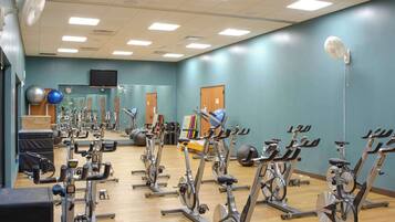 Een sportschool met meerdere hometrainers, een spiegel en diverse fitnessapparaten.