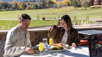 Two people dining at an outdoor table with a view of a golf course and mountains.