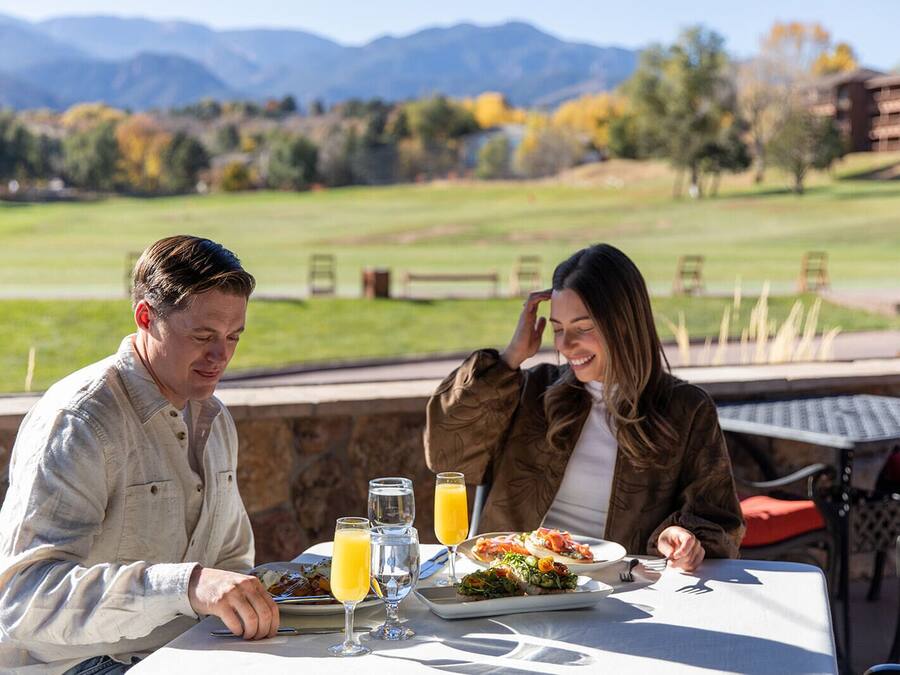 Two people dining at an outdoor table with a view of a golf course and mountains.