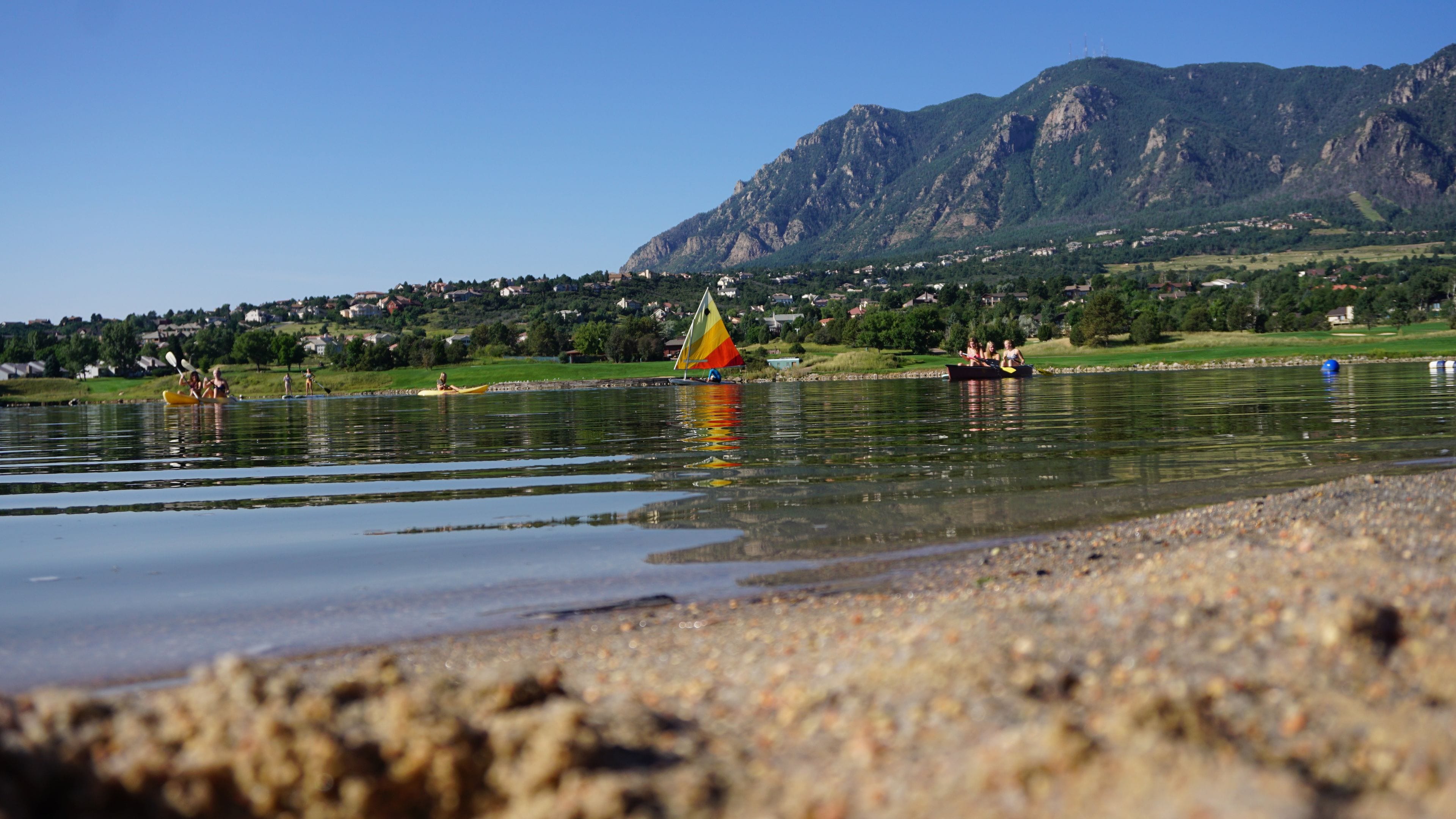 A lakeside view with a sailboat, kayaks, and a distant mountain range.
