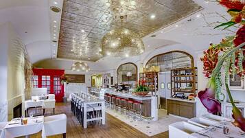 A restaurant with a high ceiling, white tables, and a bar area.