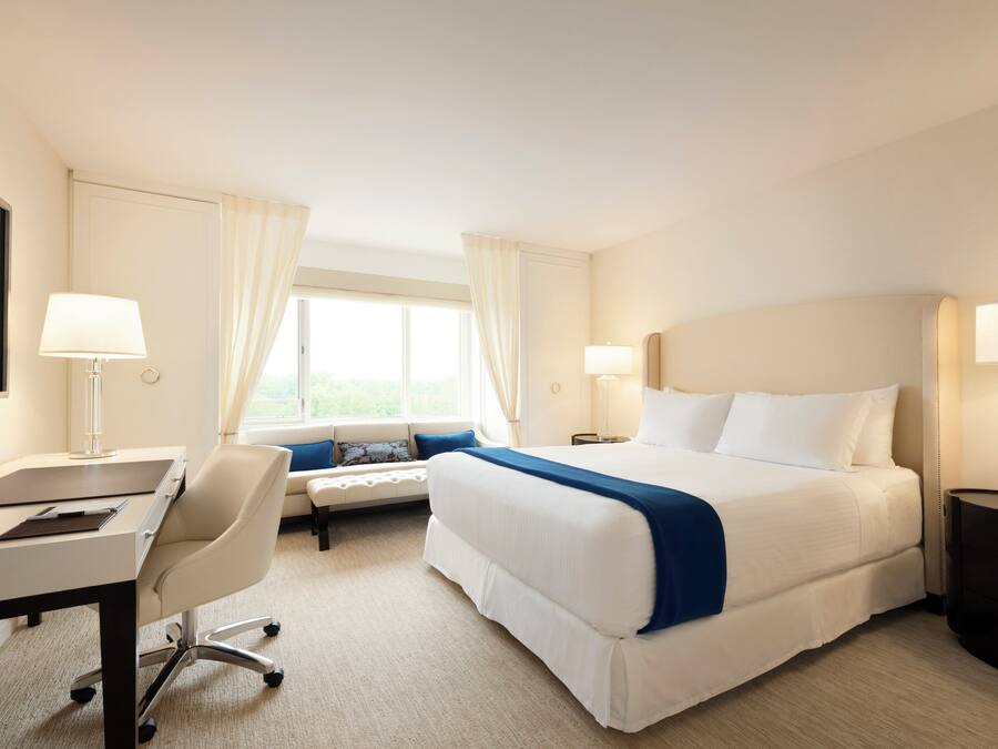 Une chambre d’hôtel avec un lit, un bureau, une chaise et un téléviseur fixé au mur.