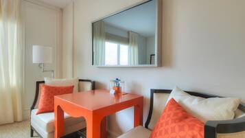 A hotel room with a sofa, a small table, a lamp, and a mirror.