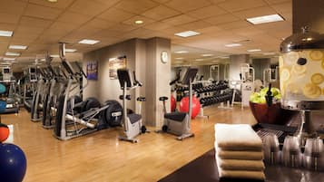 Un gimnasio con diversos equipos de ejercicio, un reloj en la pared y un dispensador de agua.