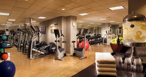 Un gimnasio con diversos equipos de ejercicio, un reloj en la pared y un dispensador de agua.