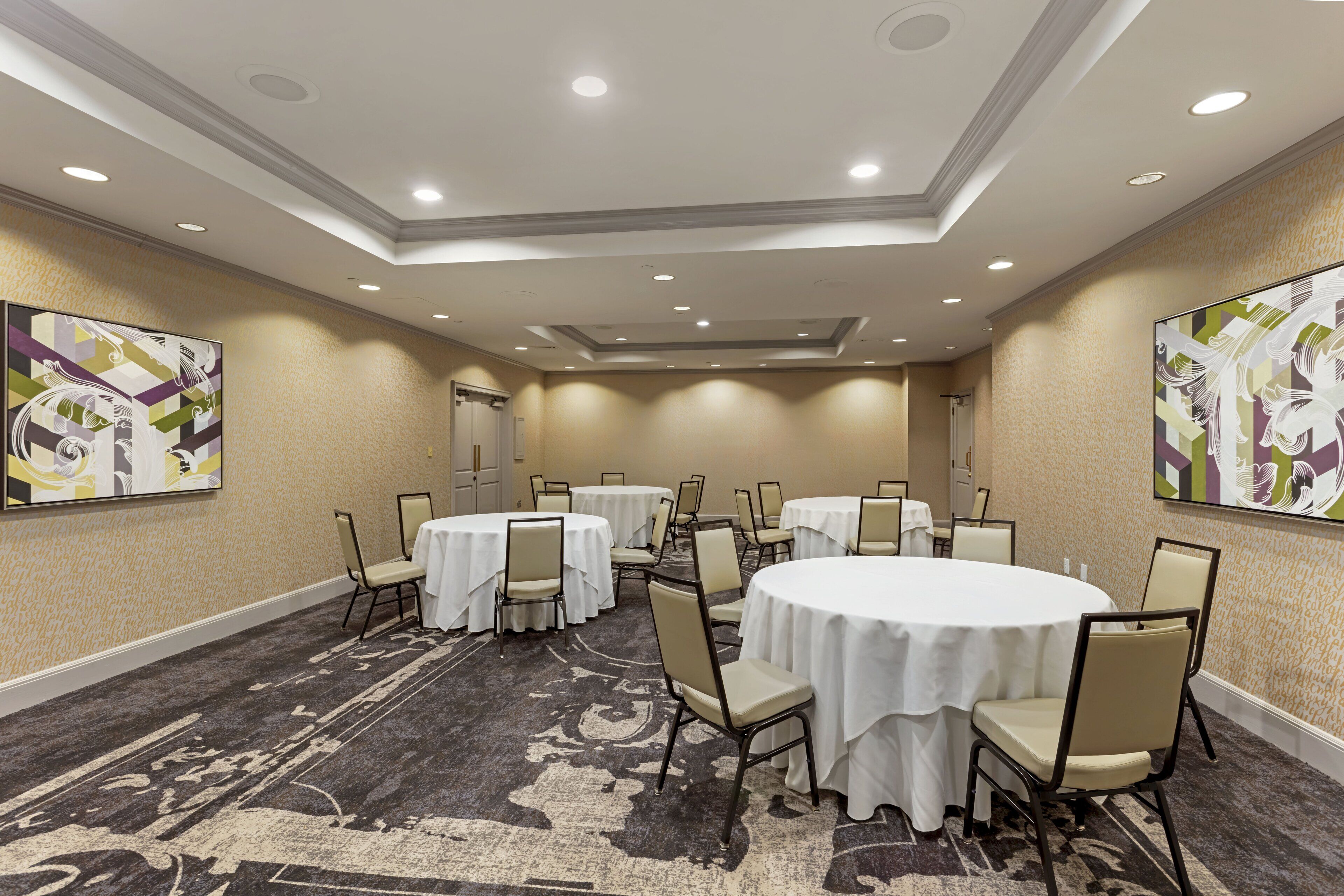 A conference room with round tables, chairs, and a carpeted floor.