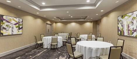 A conference room with round tables, chairs, and a carpeted floor.