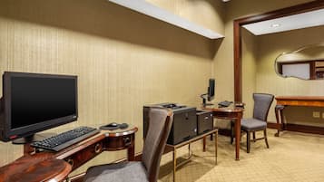 A hotel room with a desk, computer, printer, and two chairs.