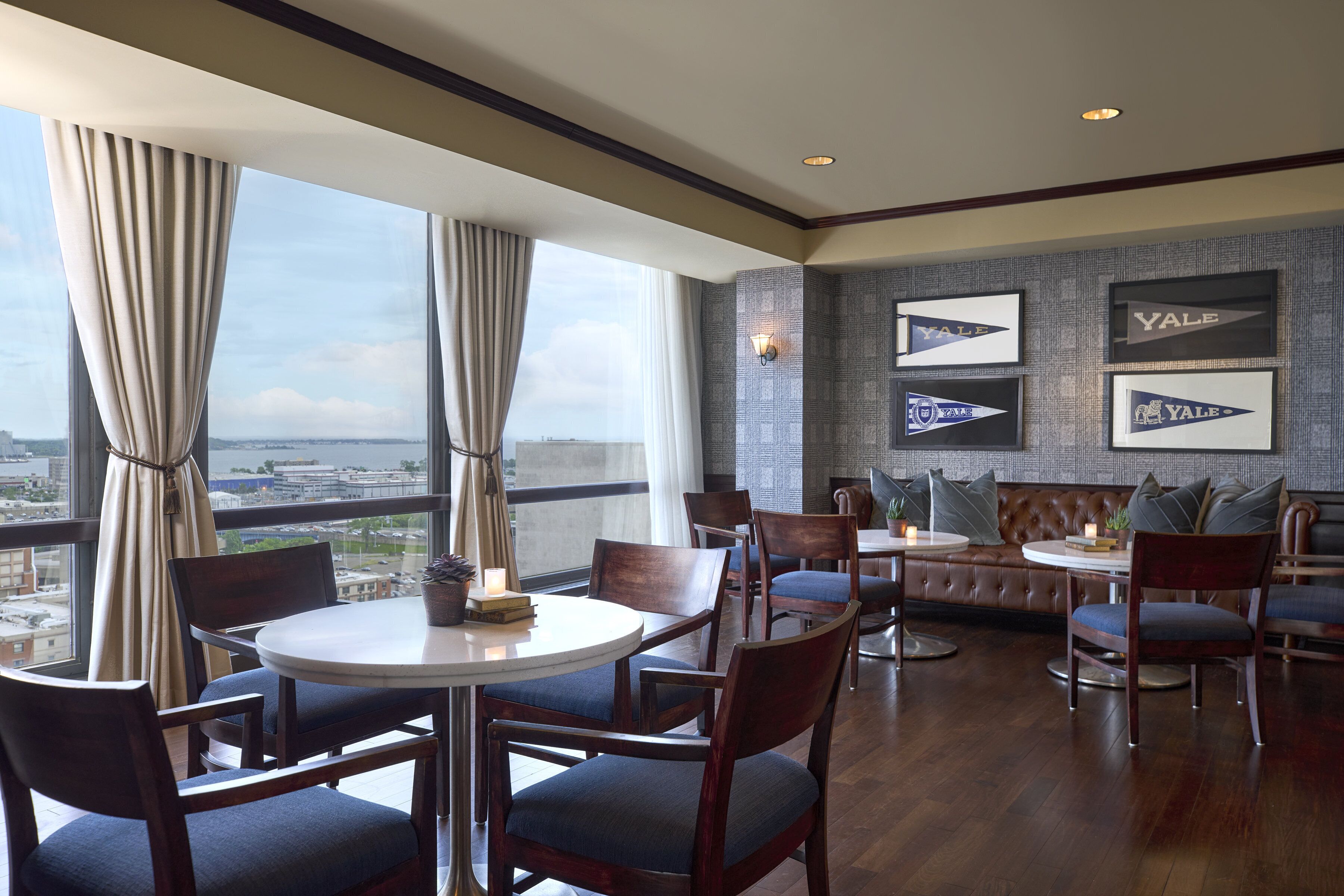 A modern dining area with round tables and chairs, a leather sofa, and framed Yale logos on the wall.