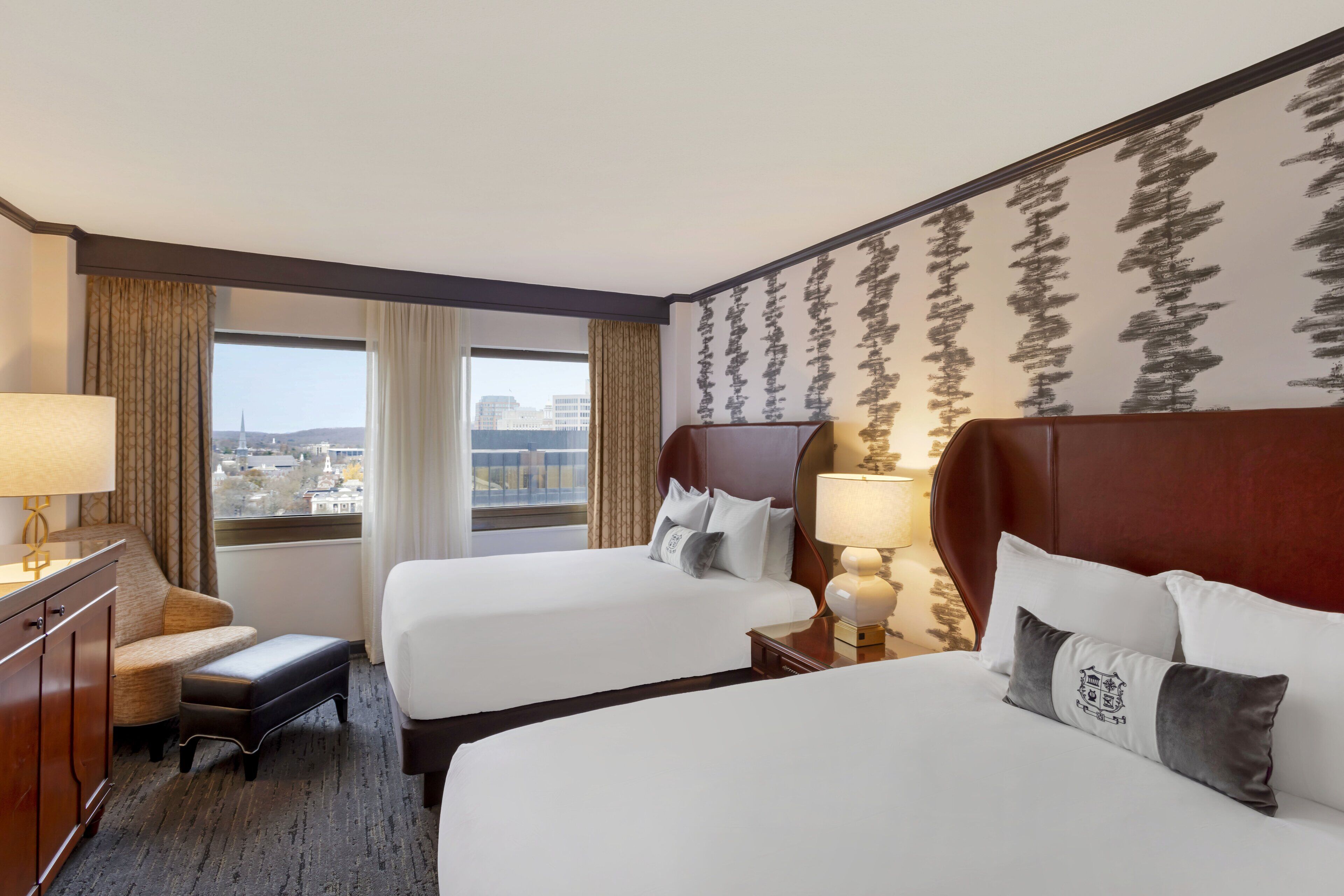 A hotel room with two beds, a desk, and a view of the city.