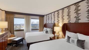 A hotel room with two beds, a desk, and a view of the city.
