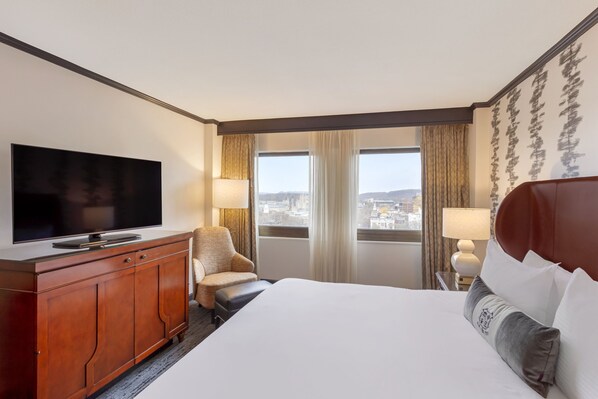 A hotel room with a large bed, a TV on a wooden cabinet, a chair, two windows with curtains, and a city view. - Omni New Haven Hotel at Yale (New Haven)