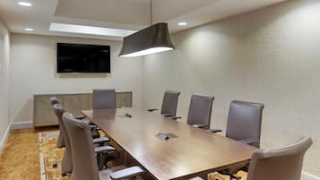 A conference room with a long table, six chairs, a flat-screen TV, and a ceiling light fixture.