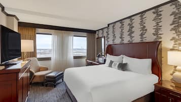 A hotel room with a large bed, a television, a desk, and a view of the city.