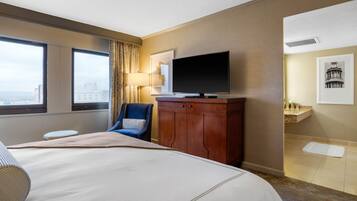 Habitación de hotel con una cama grande, televisión, una silla y vista a la ciudad.