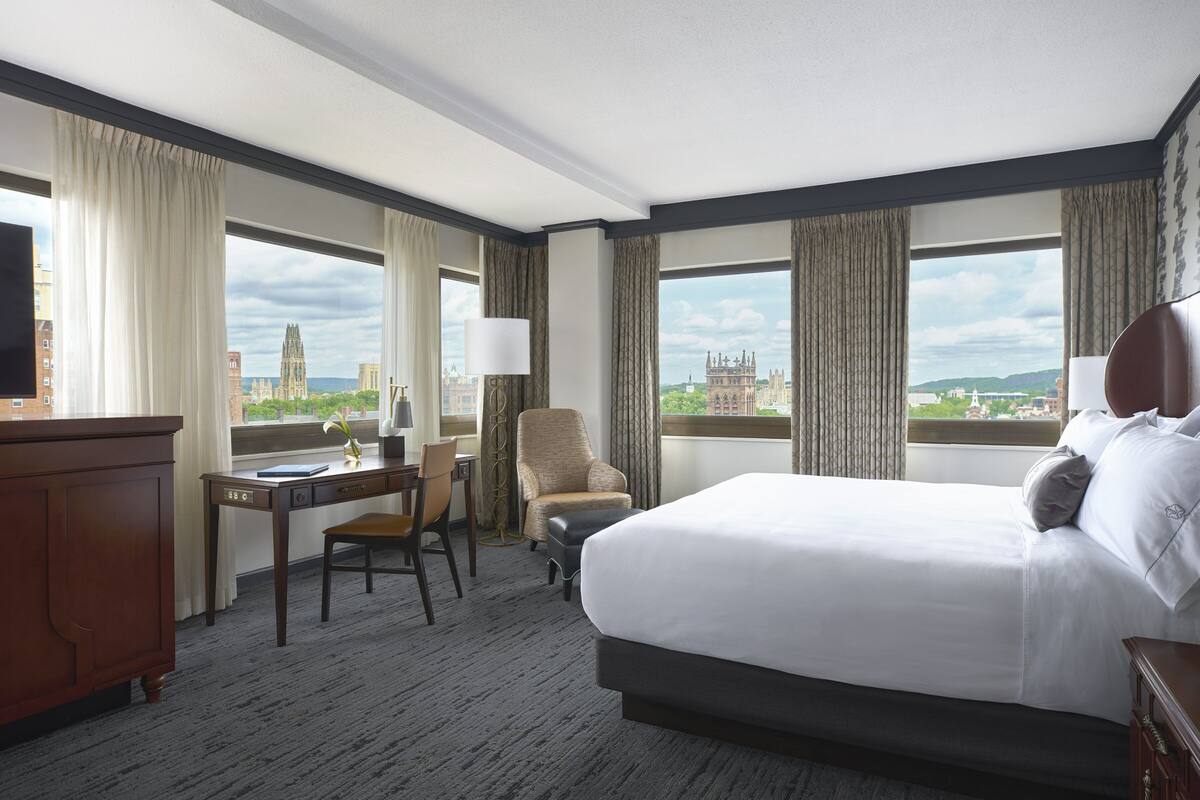 Habitación de hotel con una cama grande, un escritorio, una silla y vistas a un edificio histórico.