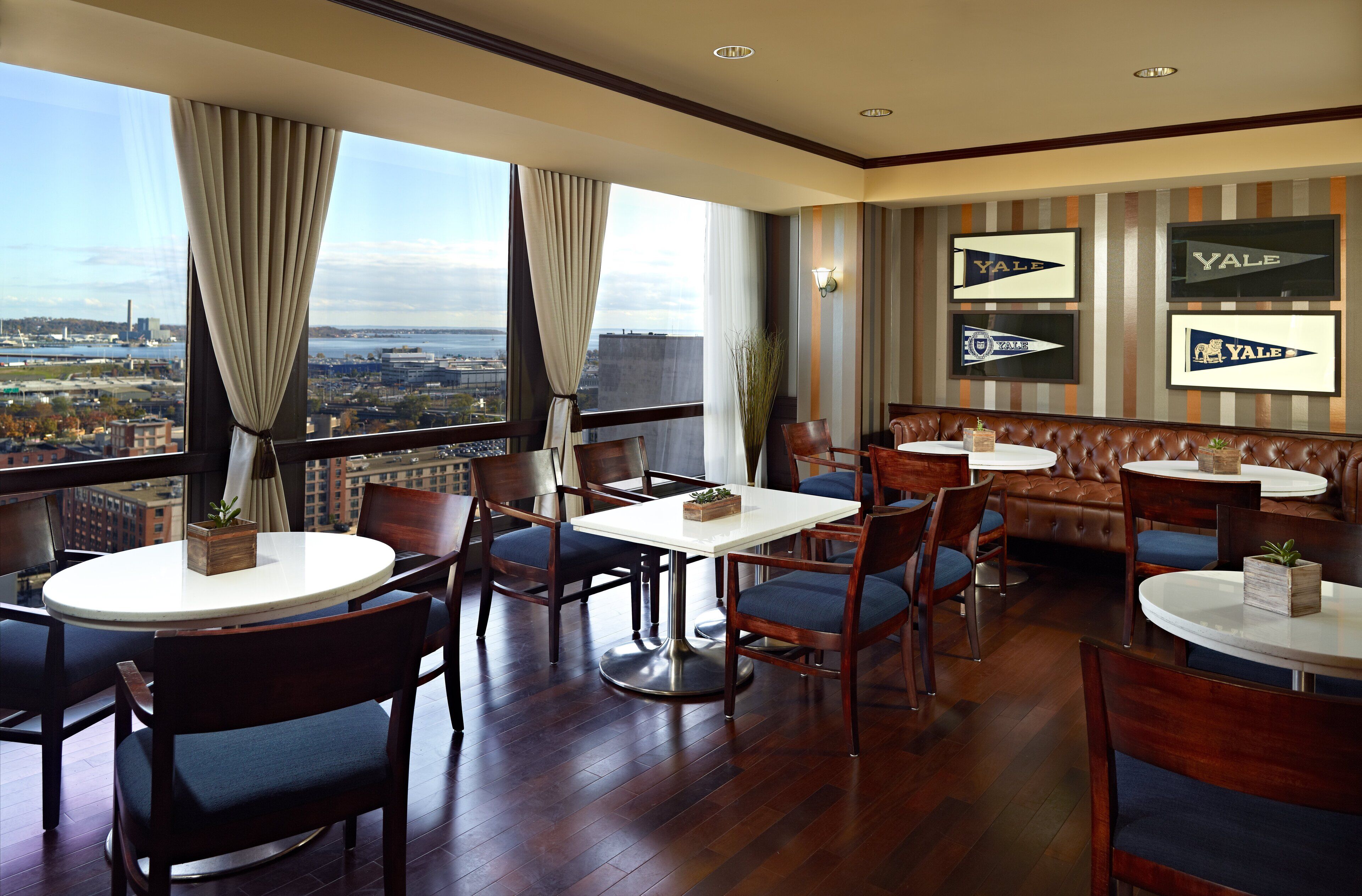 Un comedor de hotel con mesas redondas, sillas y vistas a la ciudad.