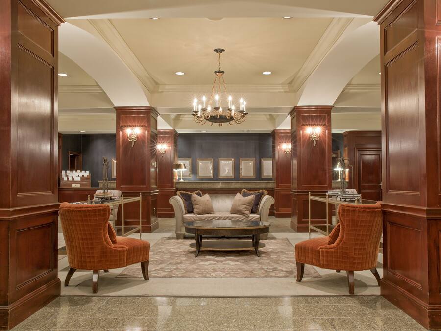 Un hall espacioso con una zona de estar central, un candelabro y paneles de madera.