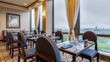 A restaurant with a city view, featuring tables set with wine glasses, plates, and napkins.