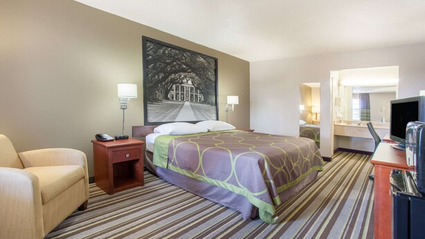 A hotel room with a bed, a chair, a desk, a television, and a painting on the wall. - Super 8 by Wyndham Monroe West (West Monroe)
