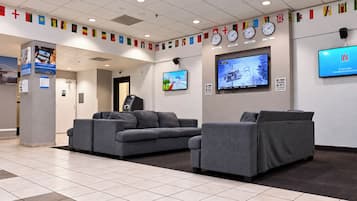 A lobby with grey sofas, a digital screen, and flags on the wall.