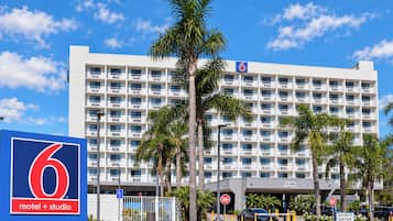 A 6 motel + studio building with a clear blue sky, palm trees, and a gated entrance.