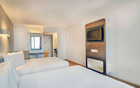 A hotel room with a large bed, a TV mounted on the wall, and a small table with a chair.