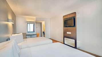 Quarto de hotel com uma cama grande, televisão fixada na parede e uma mesinha com uma cadeira.