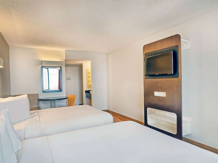 A hotel room with a large bed, a TV mounted on the wall, and a small table with a chair.