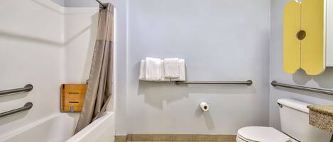 A bathroom with a bathtub, toilet, and handrails.