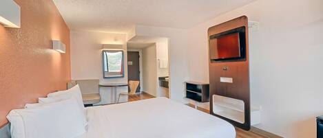 A hotel room with a large bed, a TV mounted on the wall, a small desk, and a window with a view.
