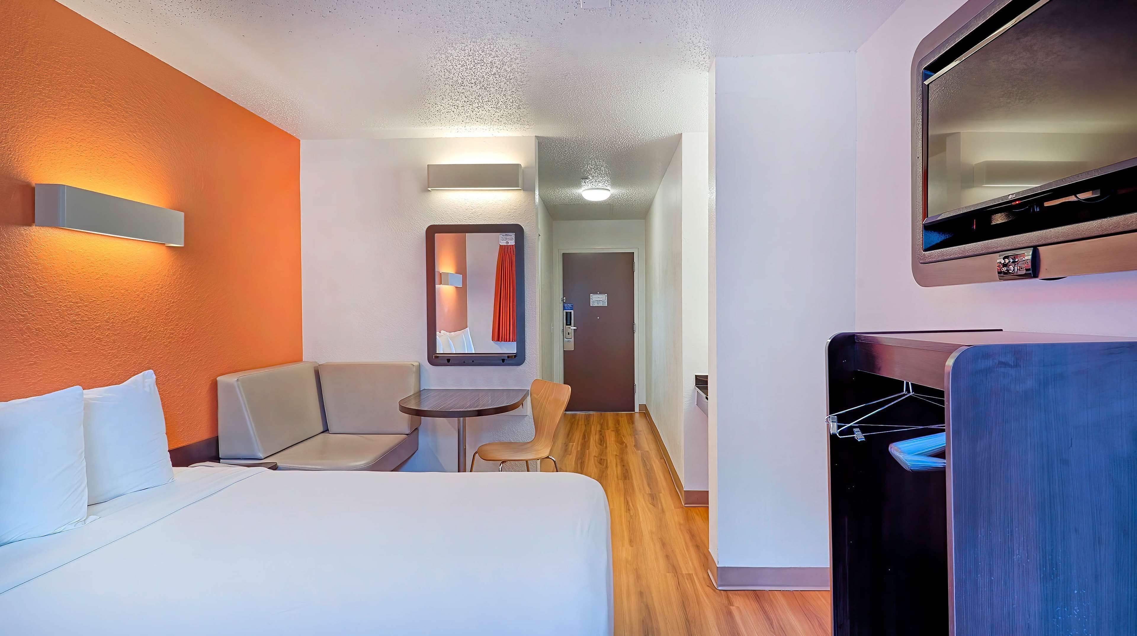 A hotel room with a bed, a seating area with a table, a mirror, and a TV mounted on the wall.
