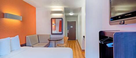 A hotel room with a bed, a seating area with a table, a mirror, and a TV mounted on the wall.