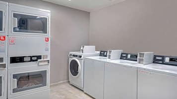 A laundry facility with stacked washing machines and dryers, a control panel, and a payment terminal.