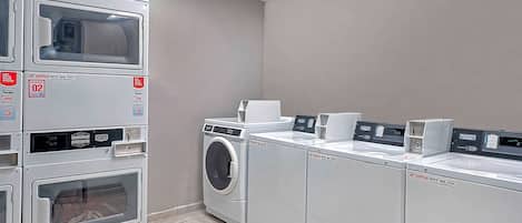 A laundry facility with stacked washing machines and dryers, a control panel, and a payment terminal.