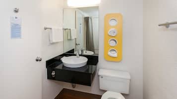 Un baño con un lavabo negro, inodoro blanco y un espejo sobre el lavabo. Se observa un perchero con una toalla blanca colgada.