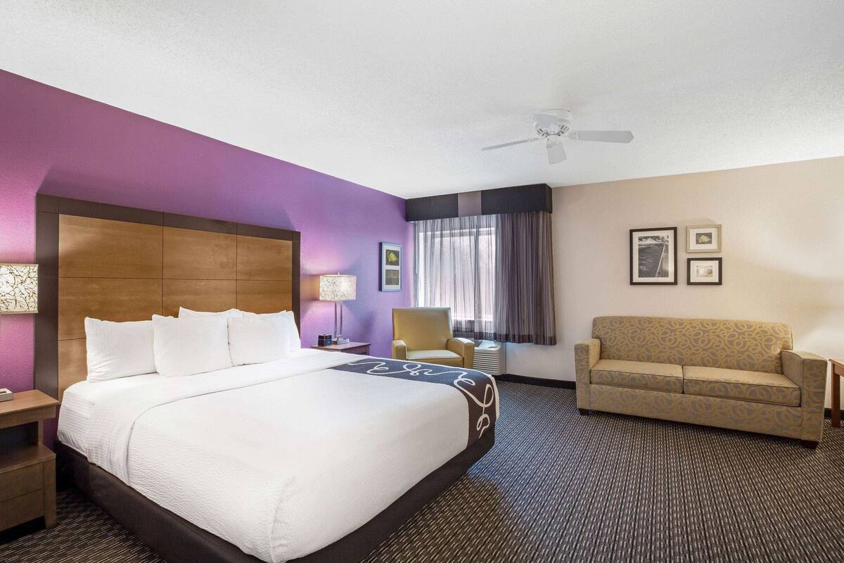Une chambre d’hôtel avec un grand lit, un canapé, un fauteuil, un bureau et un ventilateur de plafond.