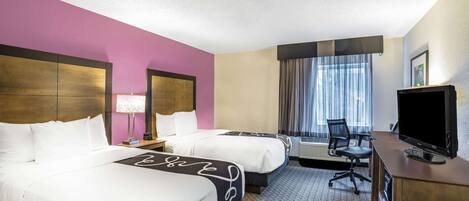 A hotel room with two beds, a desk with a TV, a chair, and a window with curtains.