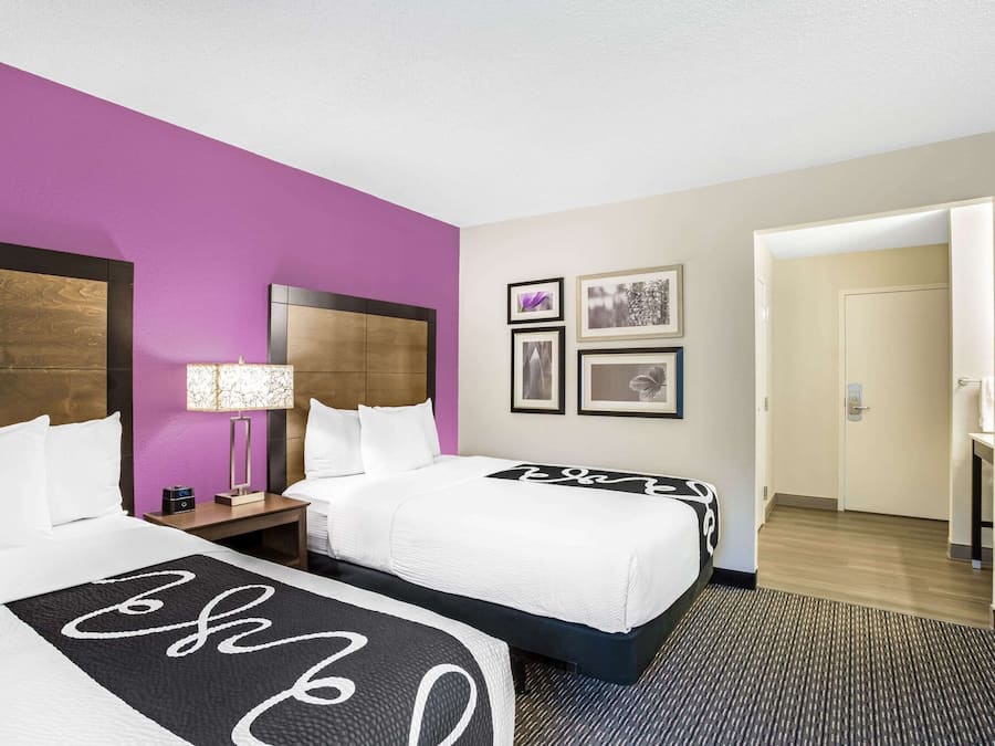 A hotel room with two beds, a nightstand, a lamp, and framed pictures on the wall.